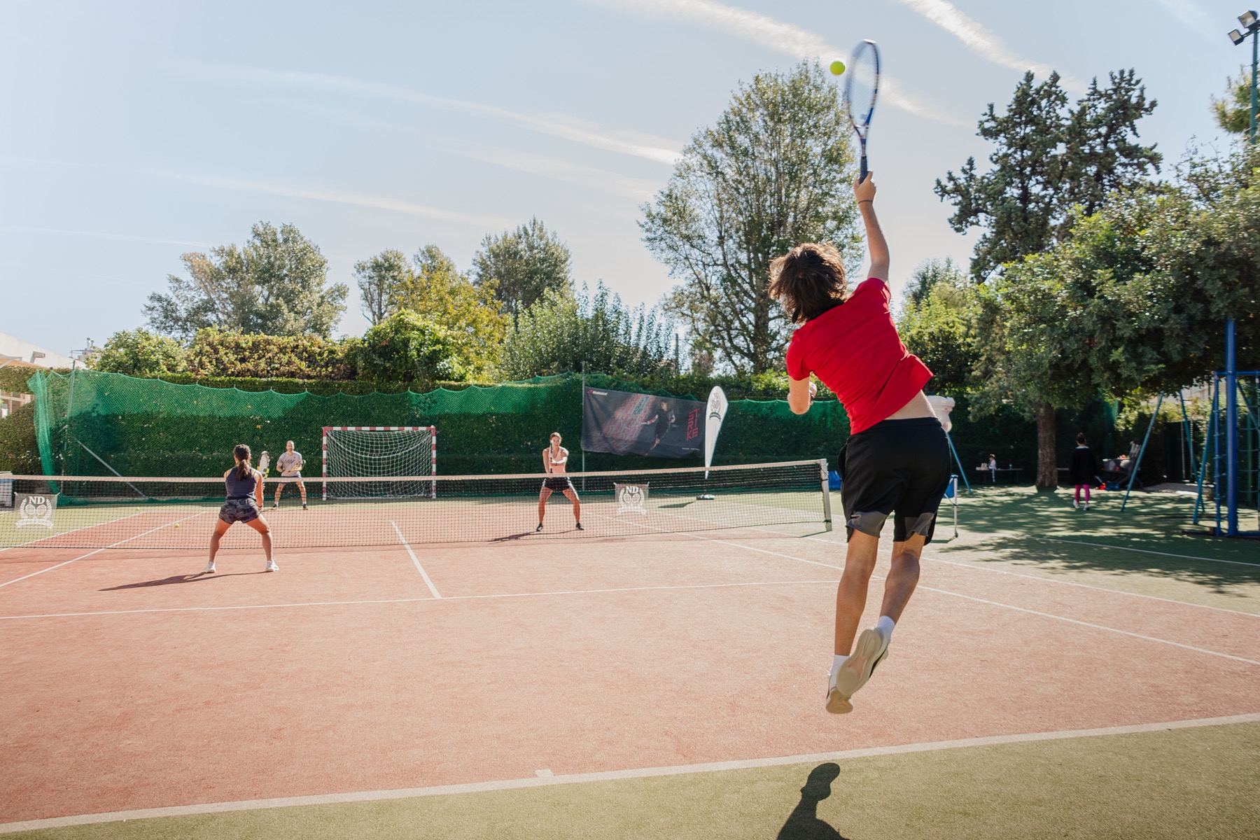 man playing tennis at nd tennis academy photo of a man in red t shirt from the back jumping to hit the ball while playing tennis